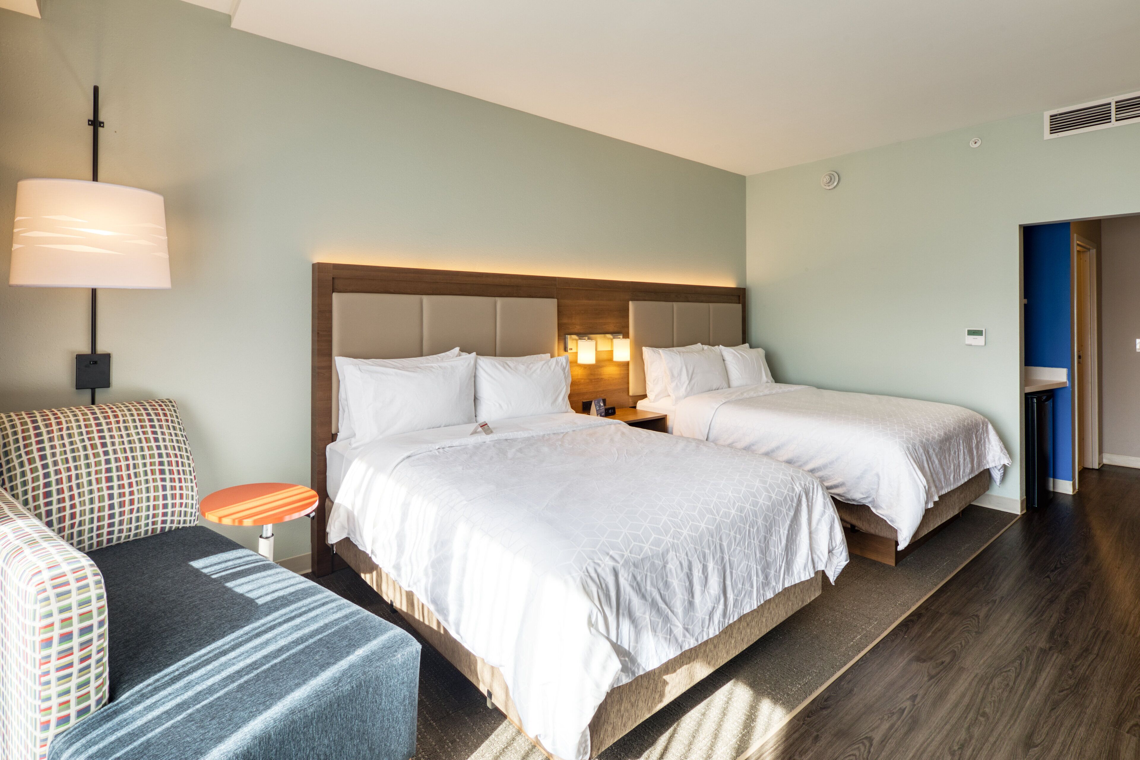 Et hotelværelse med to senge, en sofa, et lille bord og en lampe.