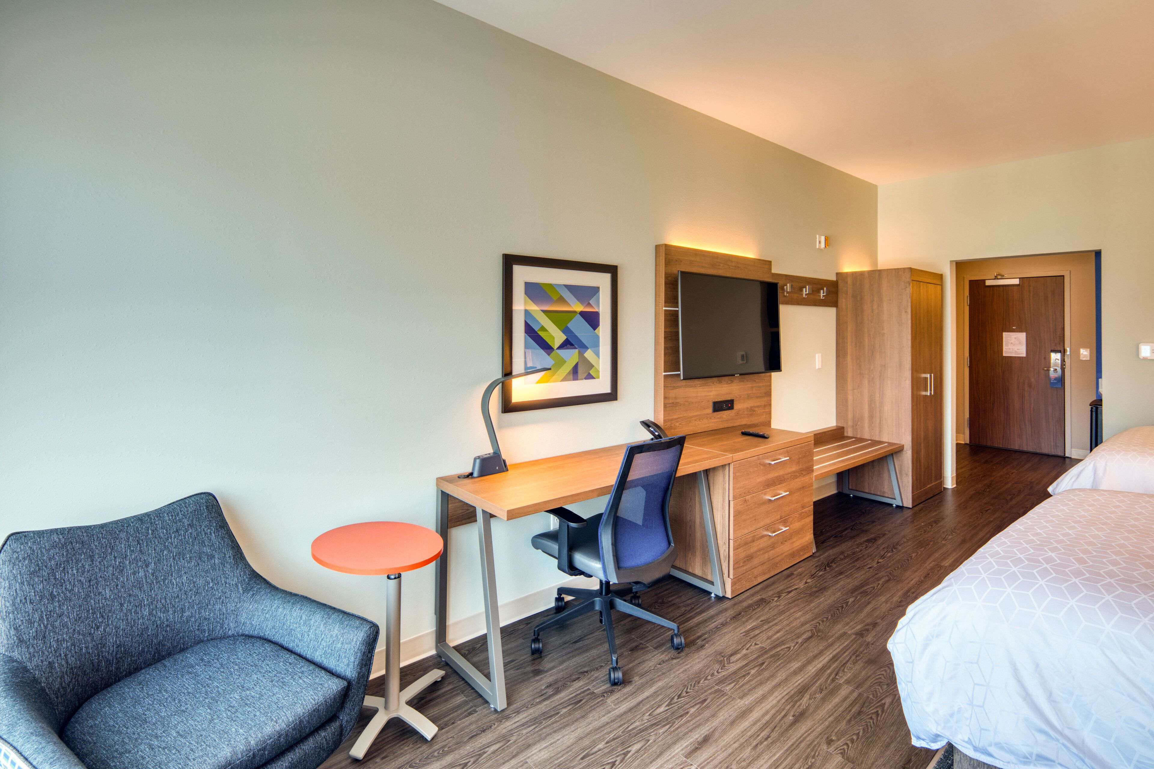 A hotel room with a desk, chair, bed, and a television.