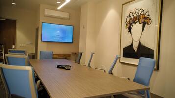 A conference room with a long table, blue chairs, a television on the wall, and a framed abstract painting.