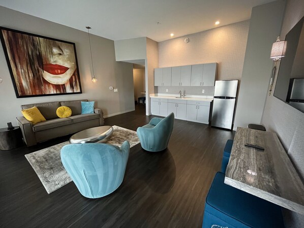 A modern living room with a sofa, two blue chairs, a coffee table, and a large abstract painting on the wall. - Holiday Inn Express & Suites Charlotte - South End by IHG (Charlotte)
