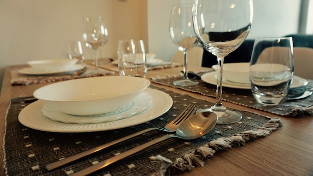 Een eettafel gedekt met borden, bestek en glazen, met een placemat eronder.