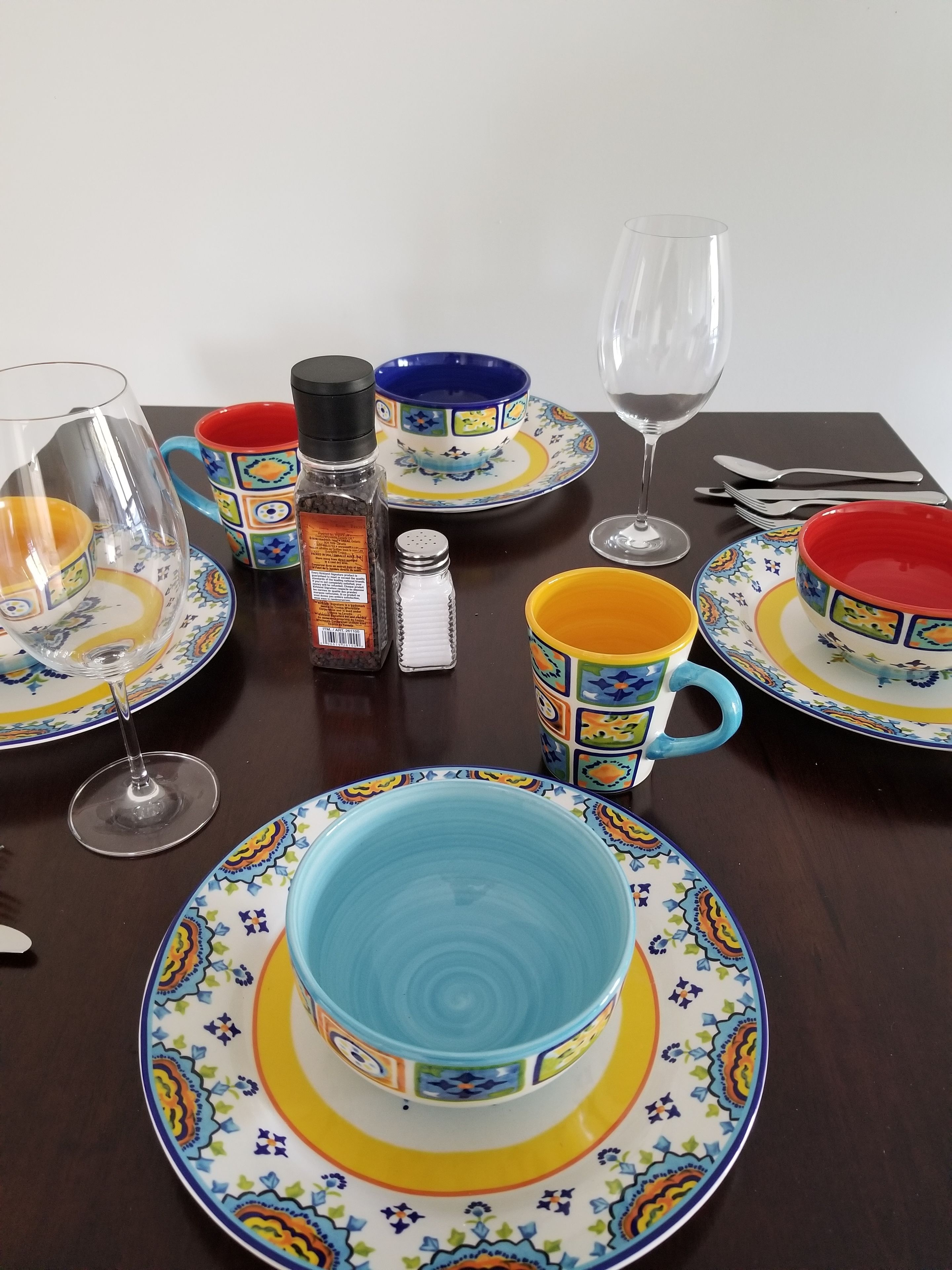Una mesa de comedor preparada con platos, tazas y una copa de vino, todo en colores vivos.