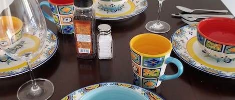 A dining table set with colorful plates, cups, and a wine glass.