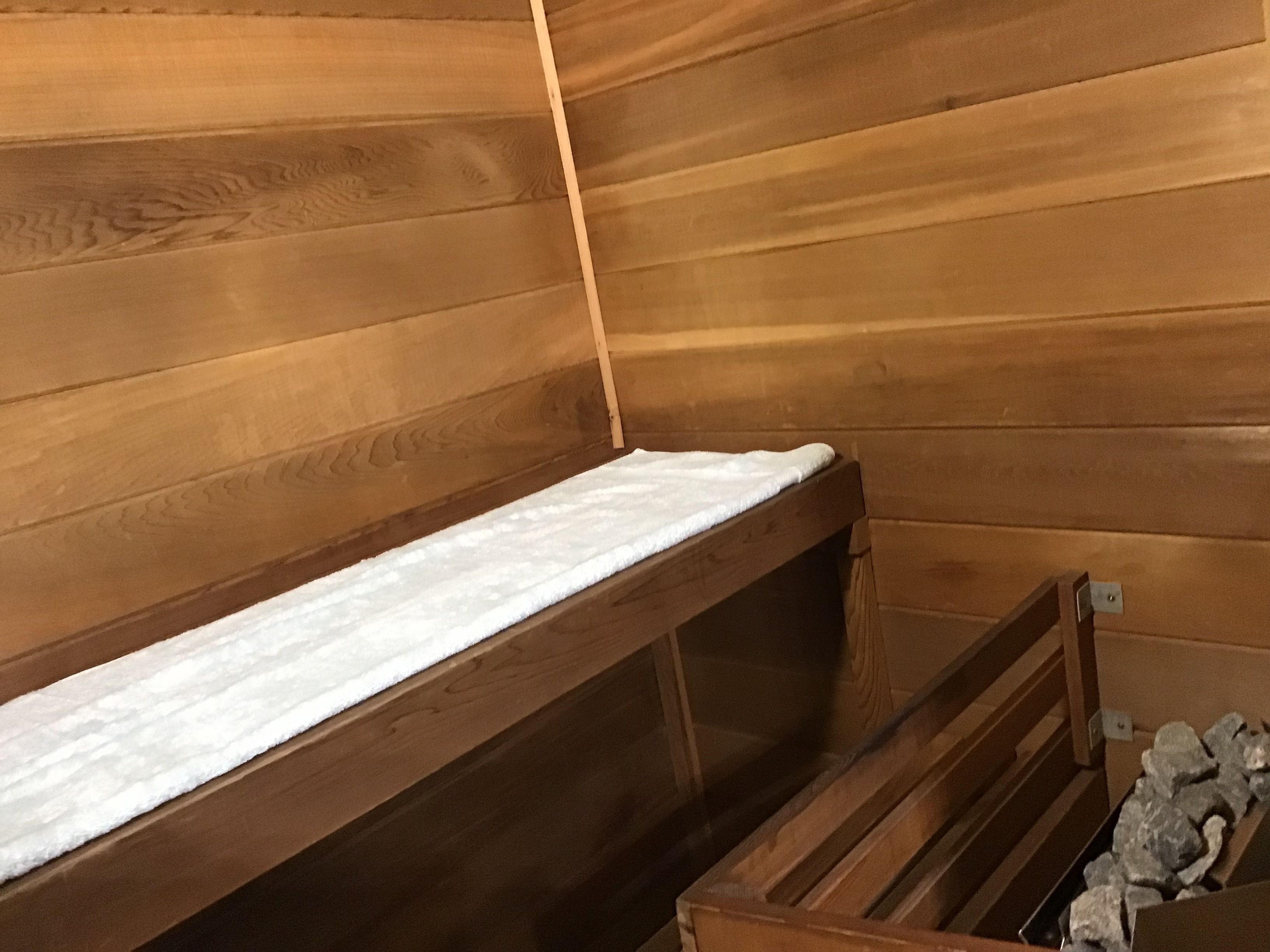 Ein Saunaraum mit Holzwänden, einer Sitzbank und einem mit Steinen gefüllten Behälter.