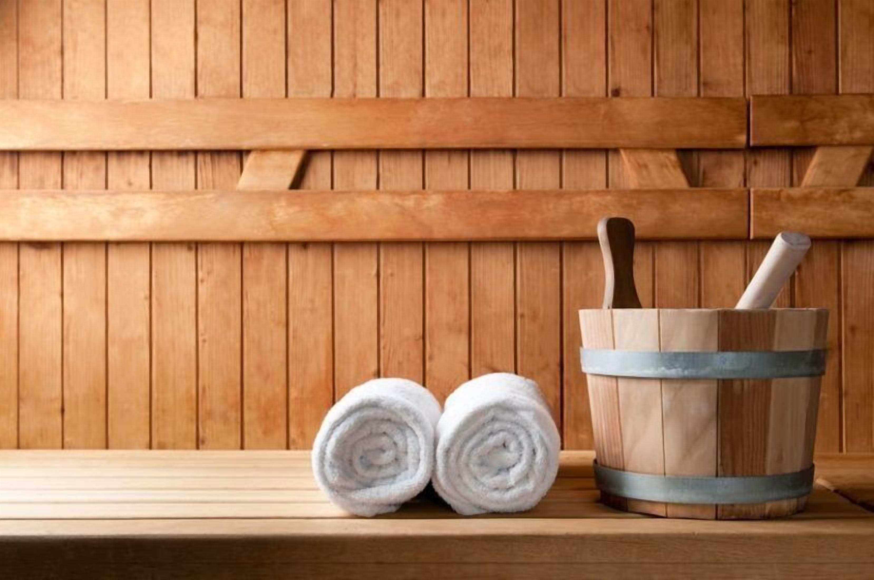 A wooden bench with two rolled white towels and a wooden bucket with a brush.