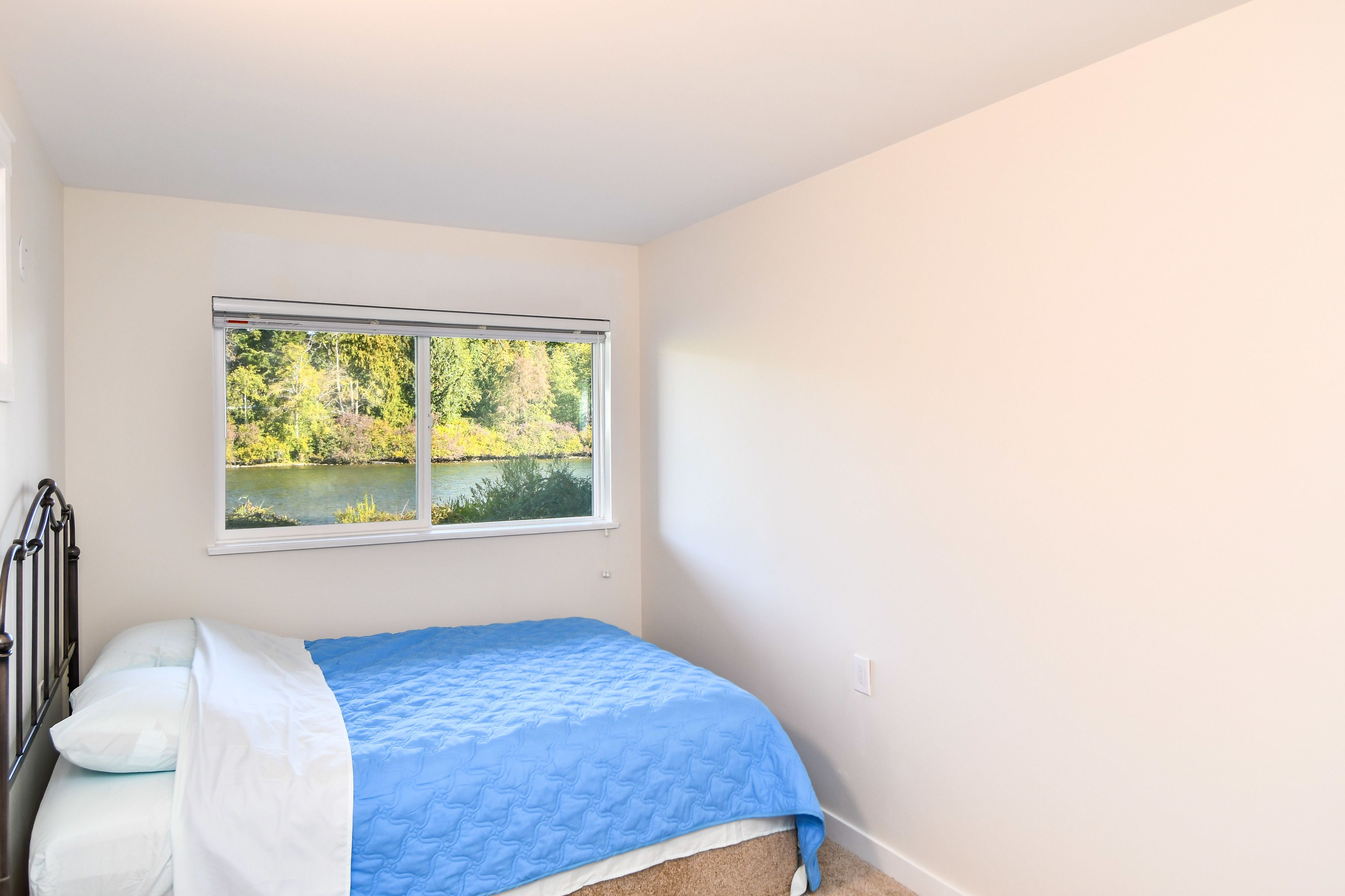 Quarto com cama, janela com vista para árvores e um corpo de água, e paredes brancas.
