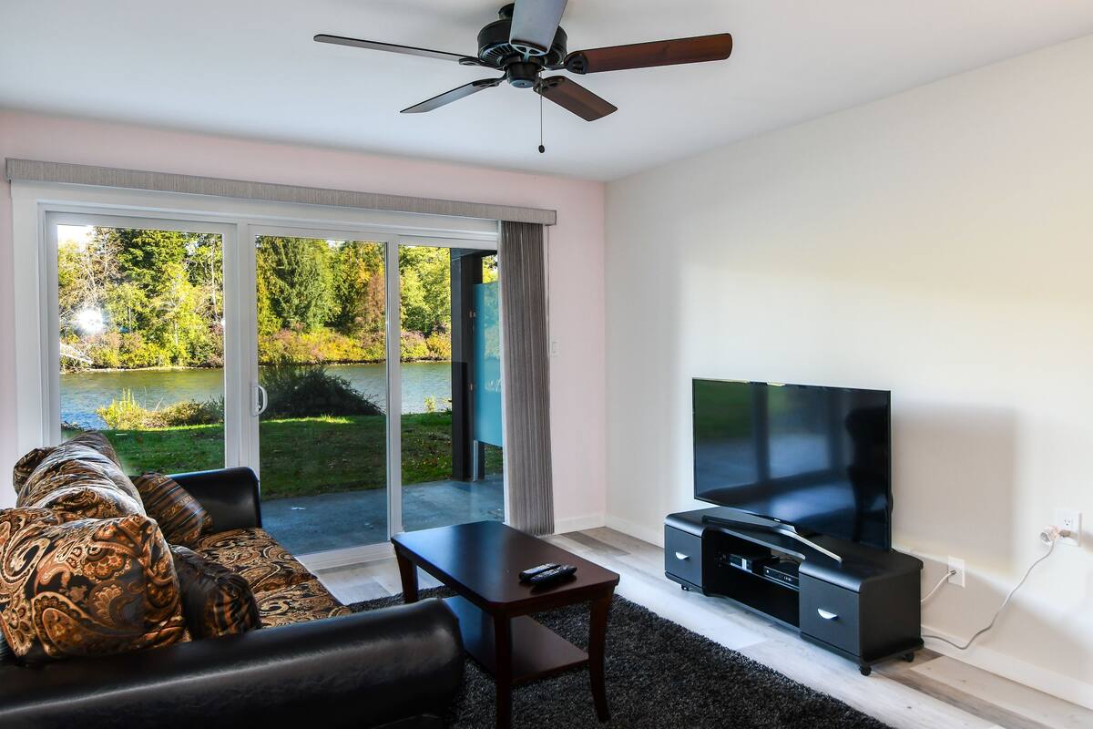 A modern living room with a large flat-screen TV, a ceiling fan, and a sofa with patterned cushions.