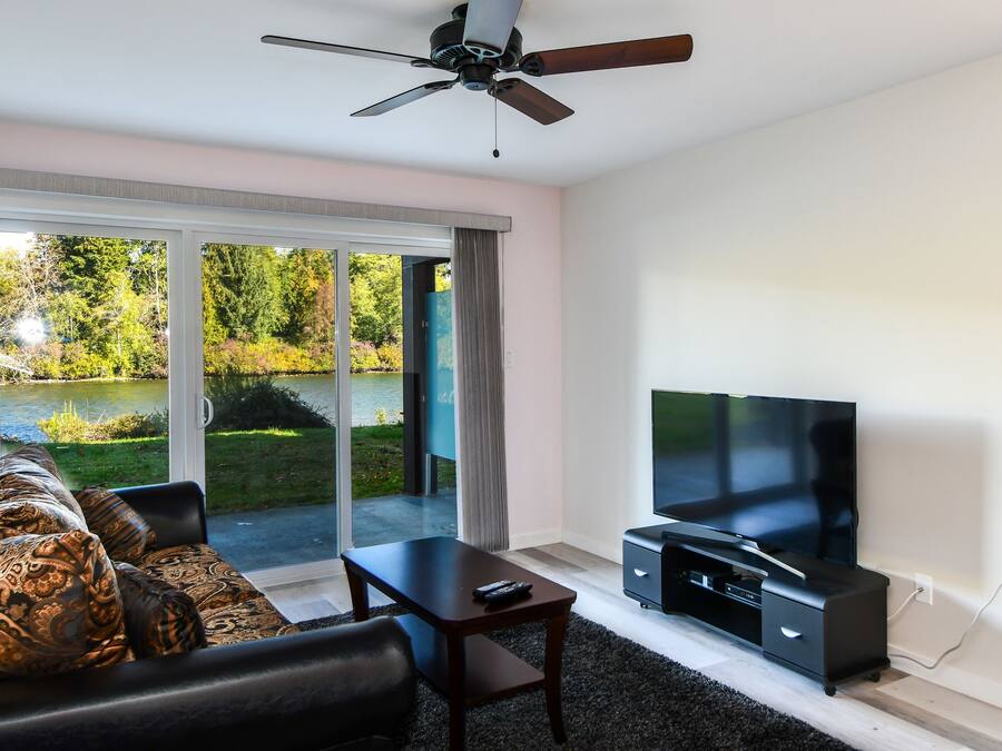 A modern living room with a large flat-screen TV, a ceiling fan, and a sofa with patterned cushions.