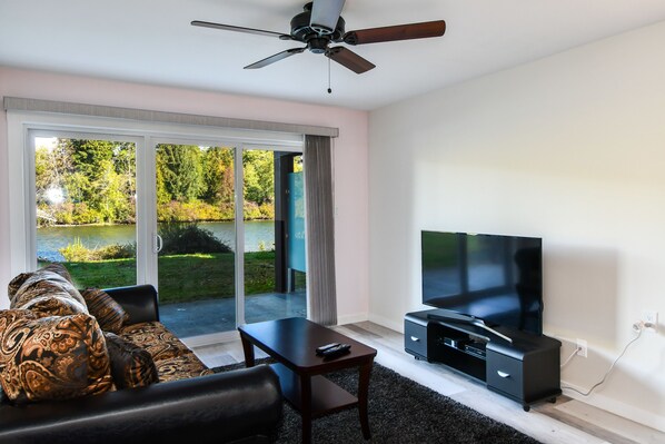 A modern living room with a large flat-screen TV, a ceiling fan, and a sofa with patterned cushions.