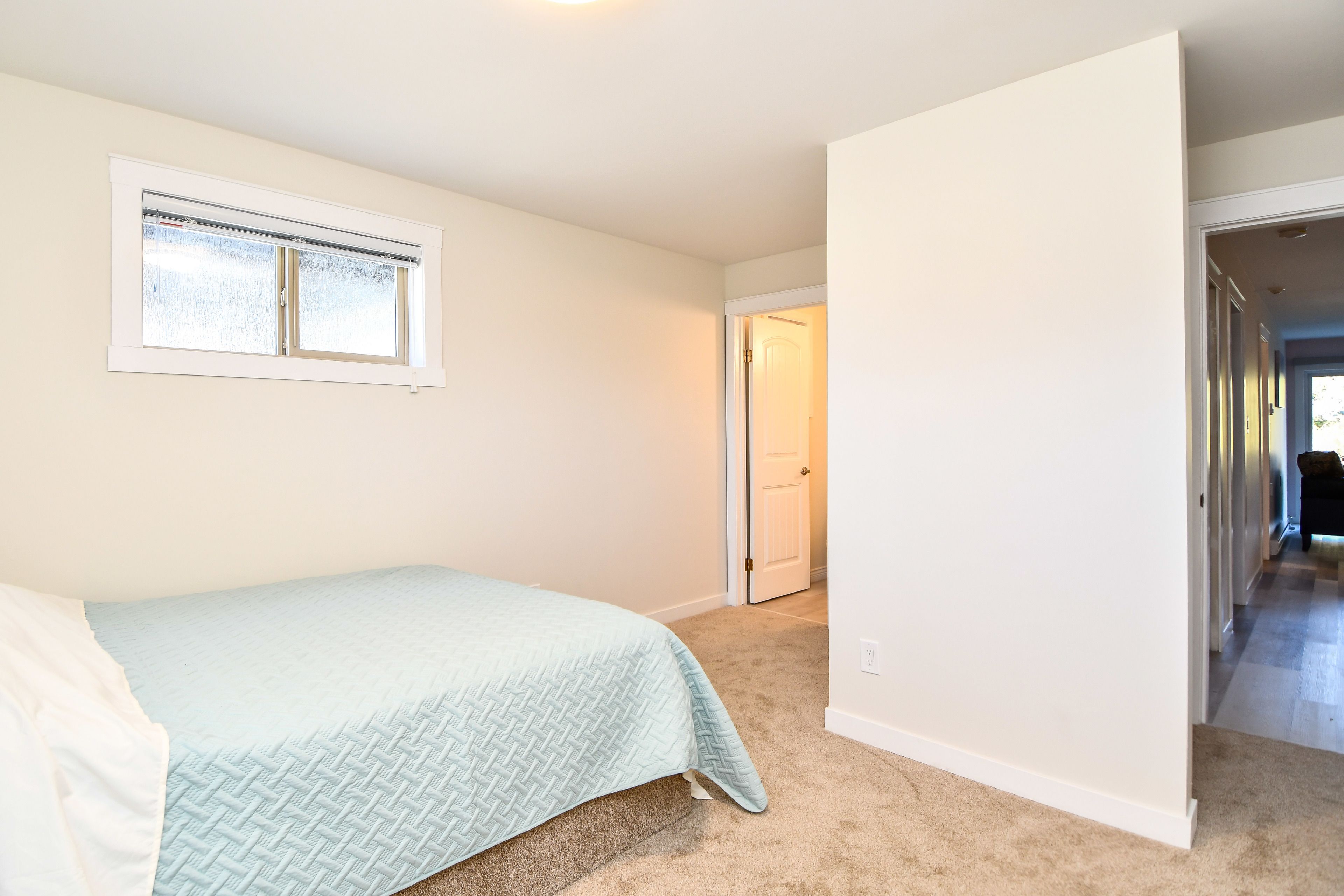 A bedroom with a bed, a window, and a door leading to another room.