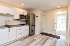 A modern kitchen with white cabinets, stainless steel appliances, and a wooden floor.