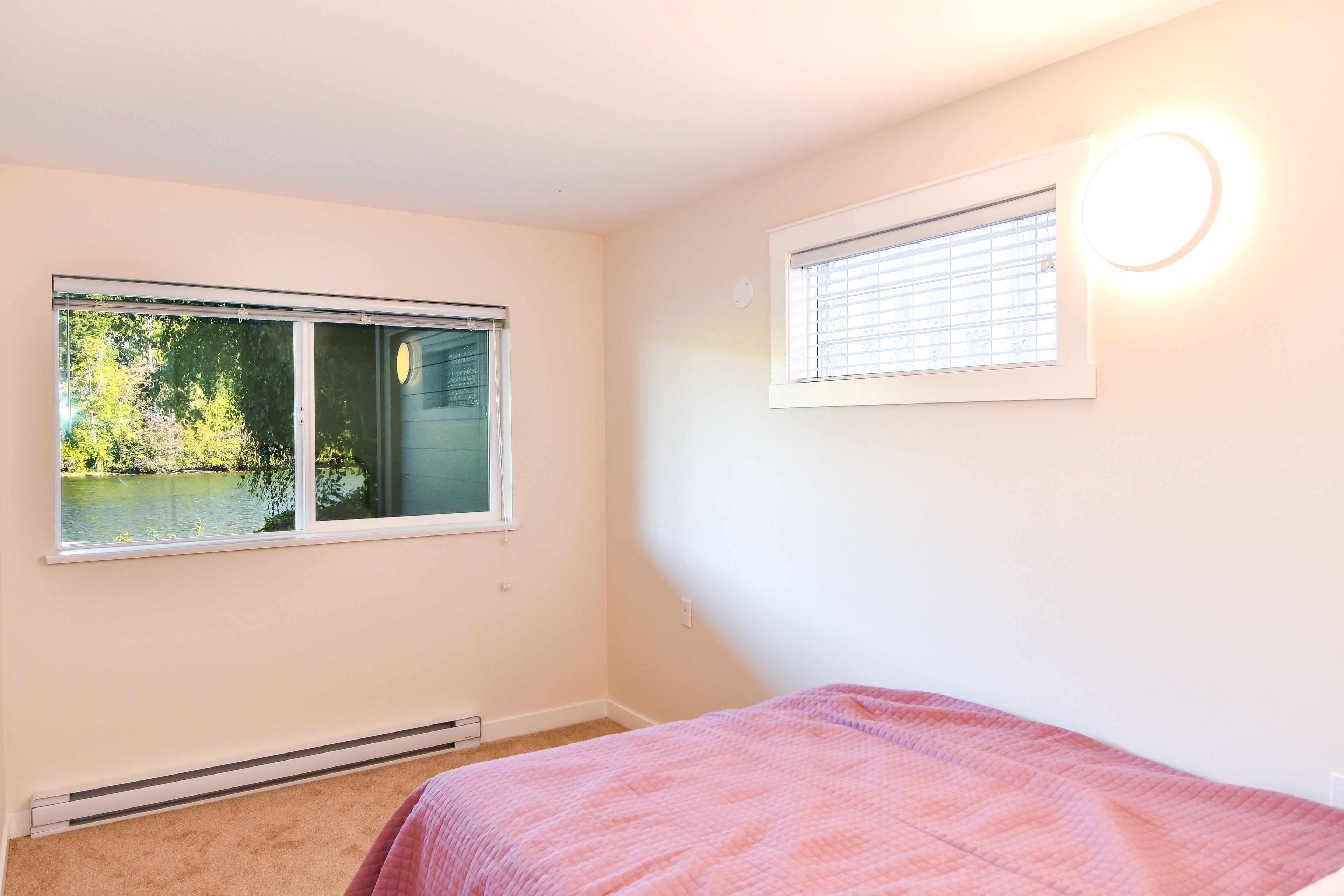 A bedroom with a large window, a bed with a pink blanket, and a wall-mounted light fixture.