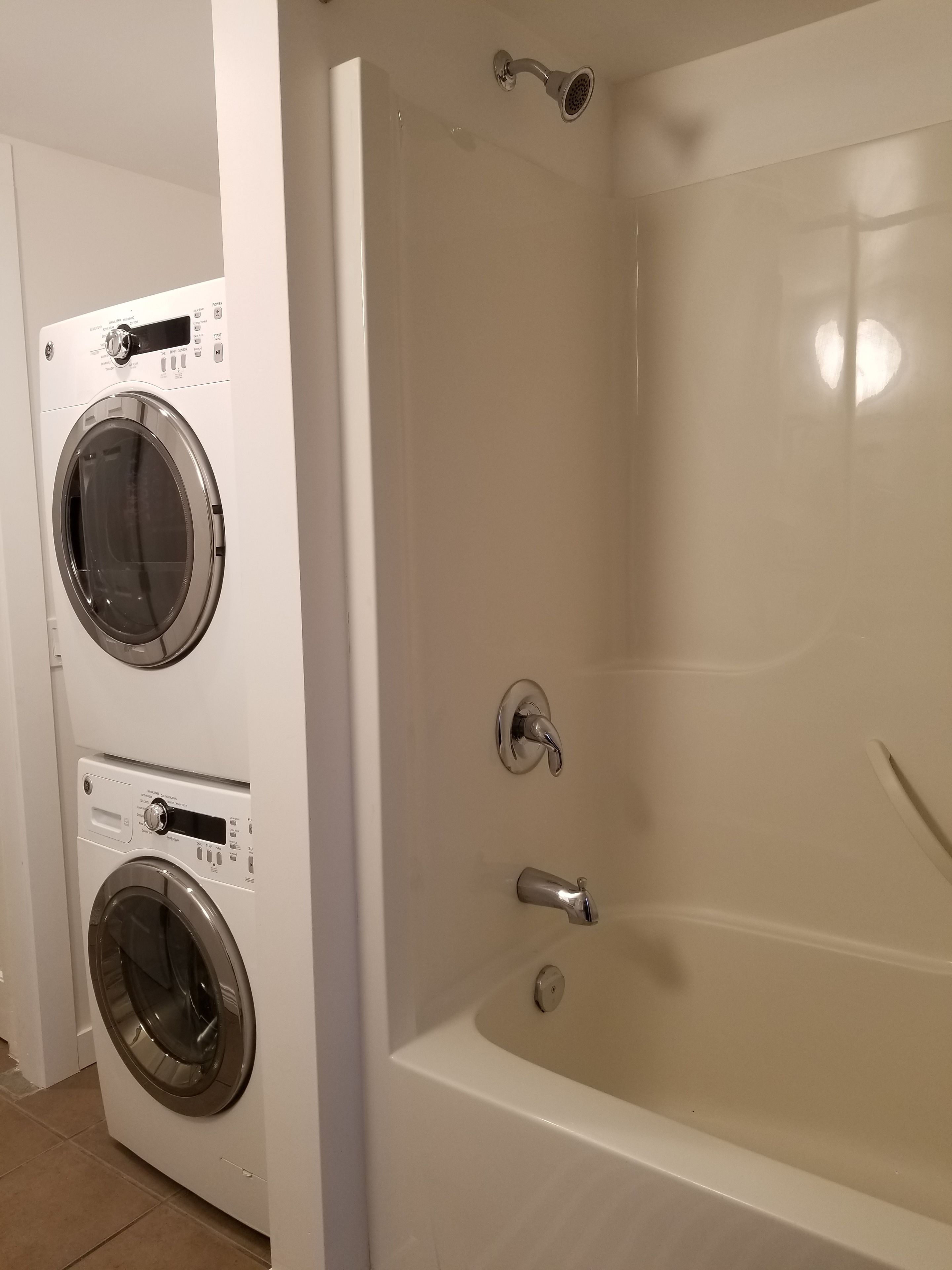 Un baño con una bañera y dos lavadoras de carga frontal.