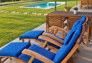 Un espace aménagé au bord de la piscine, avec des chaises longues en bois et une table.