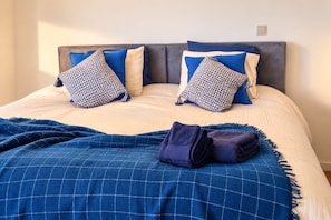 A neatly made bed with a blue checkered blanket, two patterned pillows, and a folded dark blue towel.