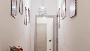 A hallway with framed pictures on the walls, a desk with a plant, and a door at the end. - Fiera051 - Affittacamere (Bologna)