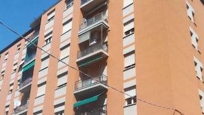 A multi-story residential building with balconies, a parking area in front, and a clear sky. - Fiera051 - Affittacamere (Bologna)