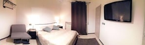 A hotel room with a bed, a chair, a desk, a lamp, a window, and a curtain. - Fiera051 - Affittacamere (Bologna)