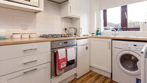 A modern kitchen with white cabinetry, a microwave, stove, oven, and a front-loading washing machine. - Sandpiper - Moments from Baiter Park (Poole)