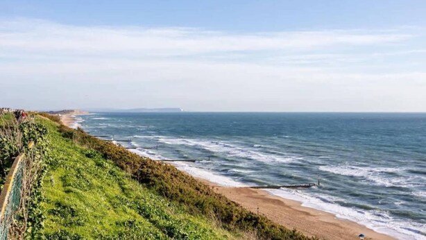 A coastal landscape with a grassy cliff, a sandy beach, and the ocean. - Sandpiper - Moments from Baiter Park (Poole)