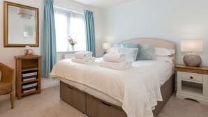 A neatly arranged bedroom with a bed, bedside tables, a chair, and a window with curtains. - Sandpiper - Moments from Baiter Park (Poole)