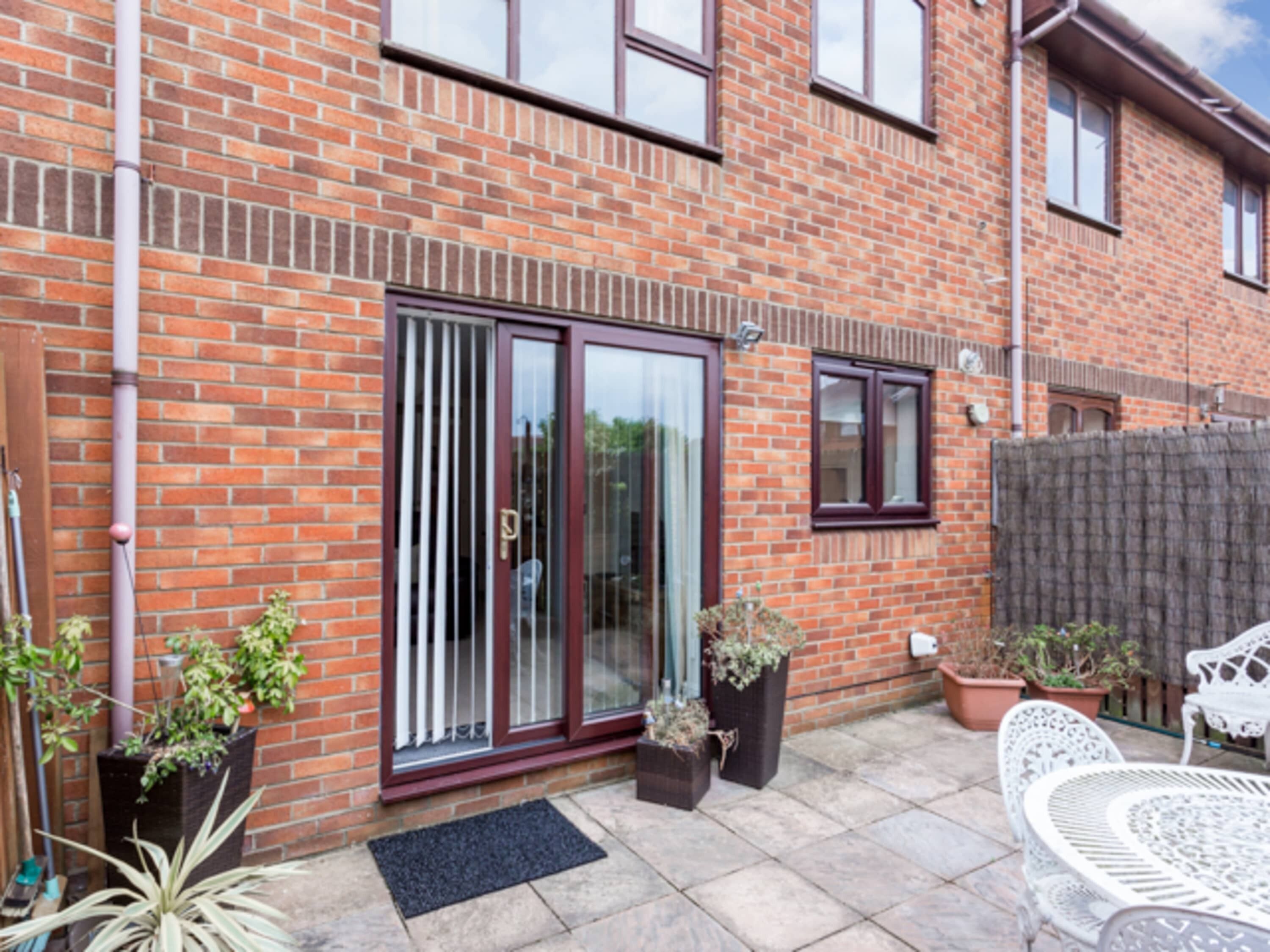 A brick house with a sliding glass door, potted plants, and outdoor furniture.