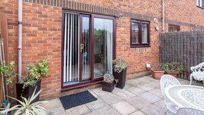 A brick house with a sliding glass door, potted plants, and outdoor furniture. - Sandpiper - Moments from Baiter Park (Poole)
