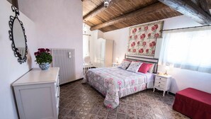 Ein Schlafzimmer mit Bett, Nachttischen, einem Schminktisch, einem Heizkörper, einem Spiegel und einer Wanddekoration mit Blumenmuster.