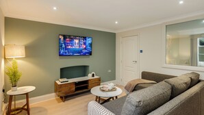 En moderne stue med et fladskærms-TV, en sofa, et sofabord og et lille sofabord med en lampe.