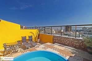 Enjoy breathtaking city views from this rooftop terrace featuring a pool, wicker chairs, and a table.
