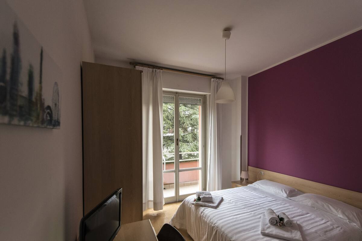 Une chambre d’hôtel avec un lit, un bureau, une chaise, une fenêtre avec des rideaux et un tableau au mur.