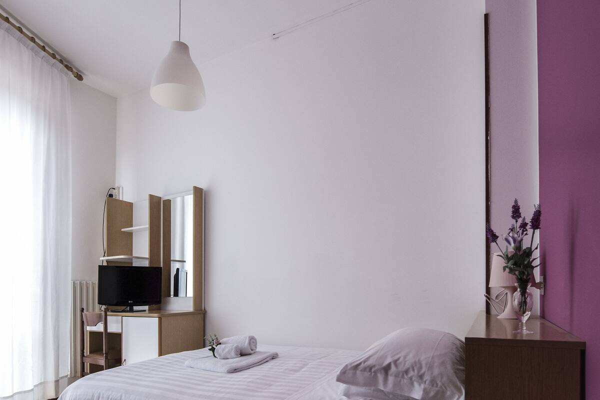 Une chambre moderne avec un lit, un bureau, une télévision et un luminaire suspendu.