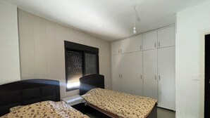 A bedroom with two beds, a window with blinds, a wardrobe, and a bedside table. - Apartment in Jdeideh Beirut (Jdeideh)