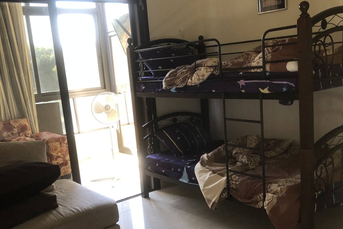 A dormitory room with bunk beds, a sofa, and a fan.