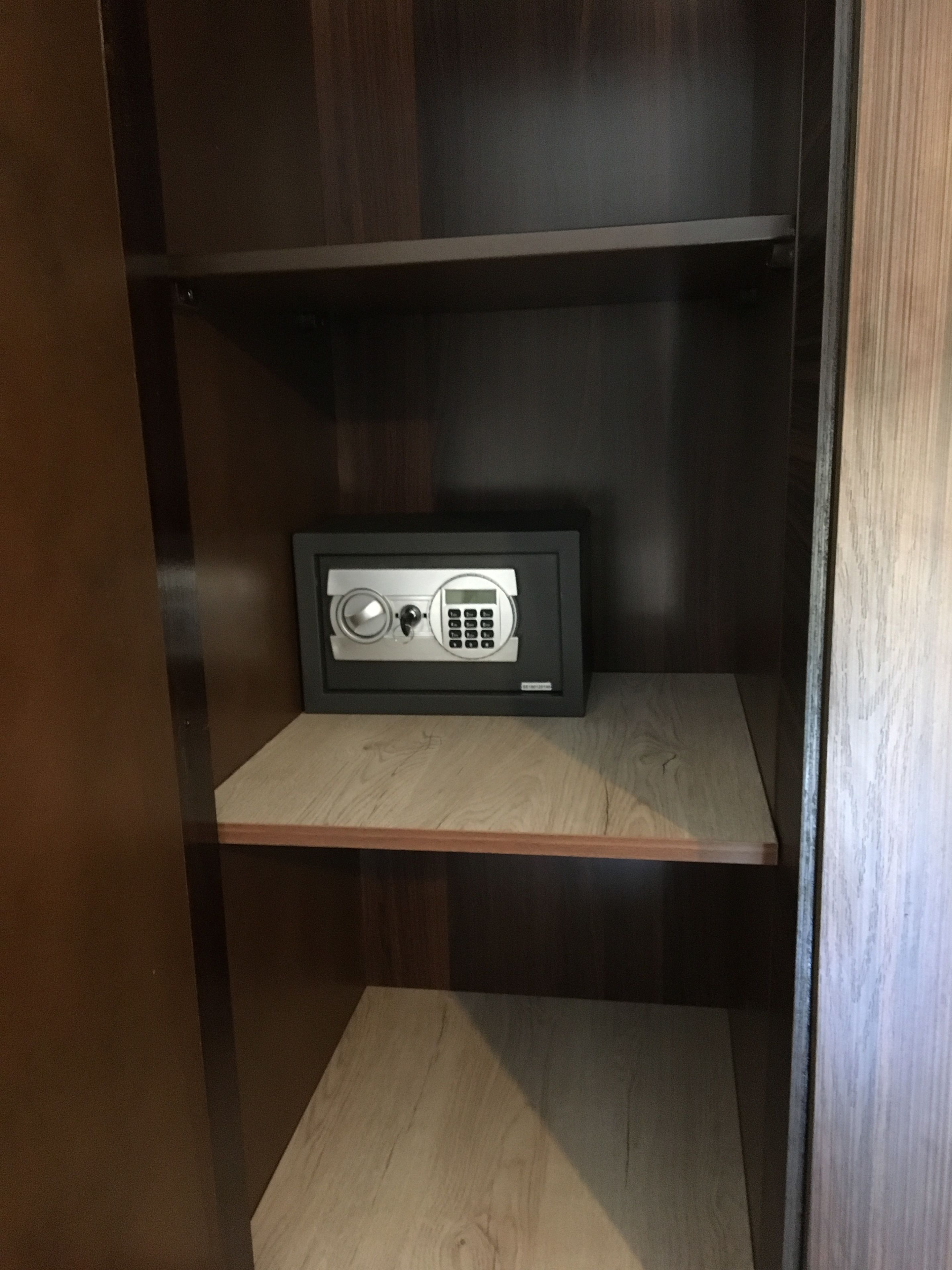 A safe deposit box with a combination dial and keypad, located on a wooden shelf in a dark wooden cabinet.