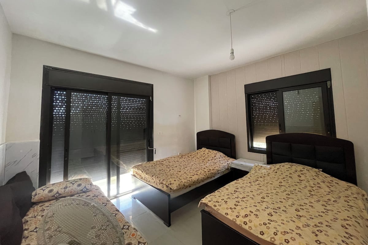 A room with two beds, a large window, and a sliding glass door.