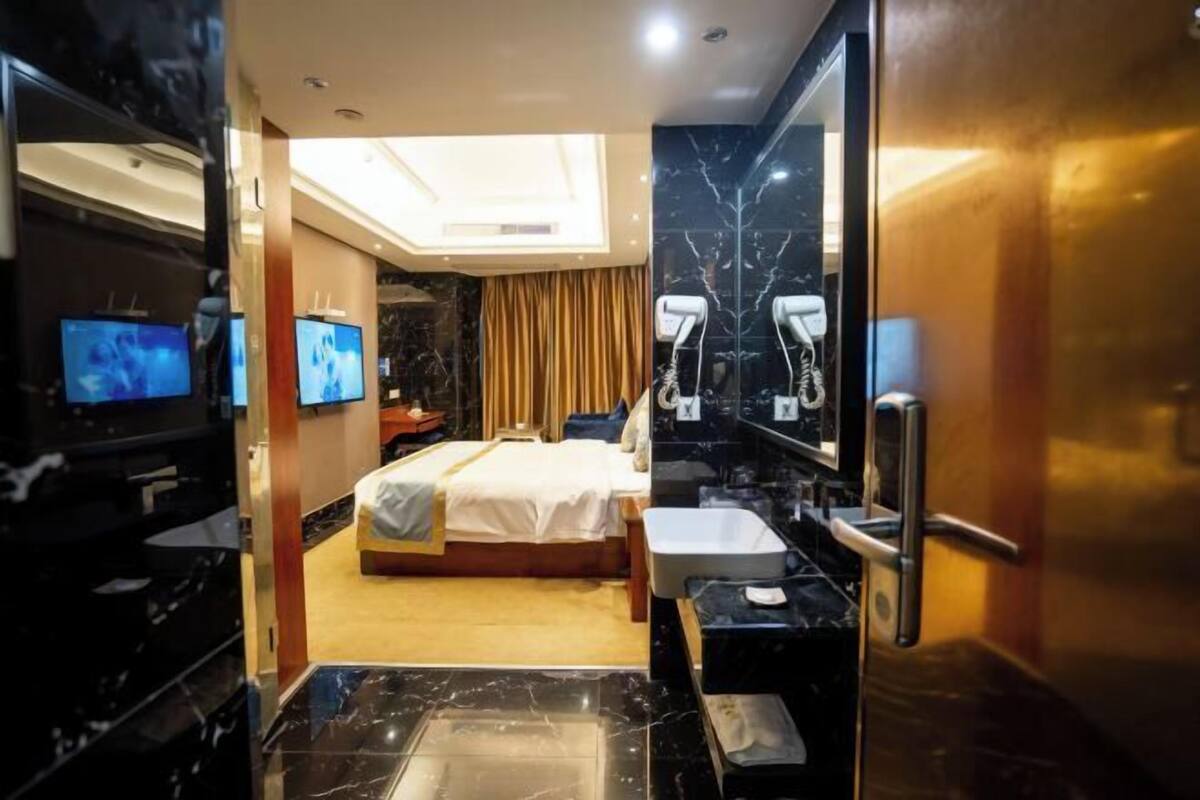 A hotel room with a bed, a large mirror, a TV, and a bathroom with a sink and mirror.