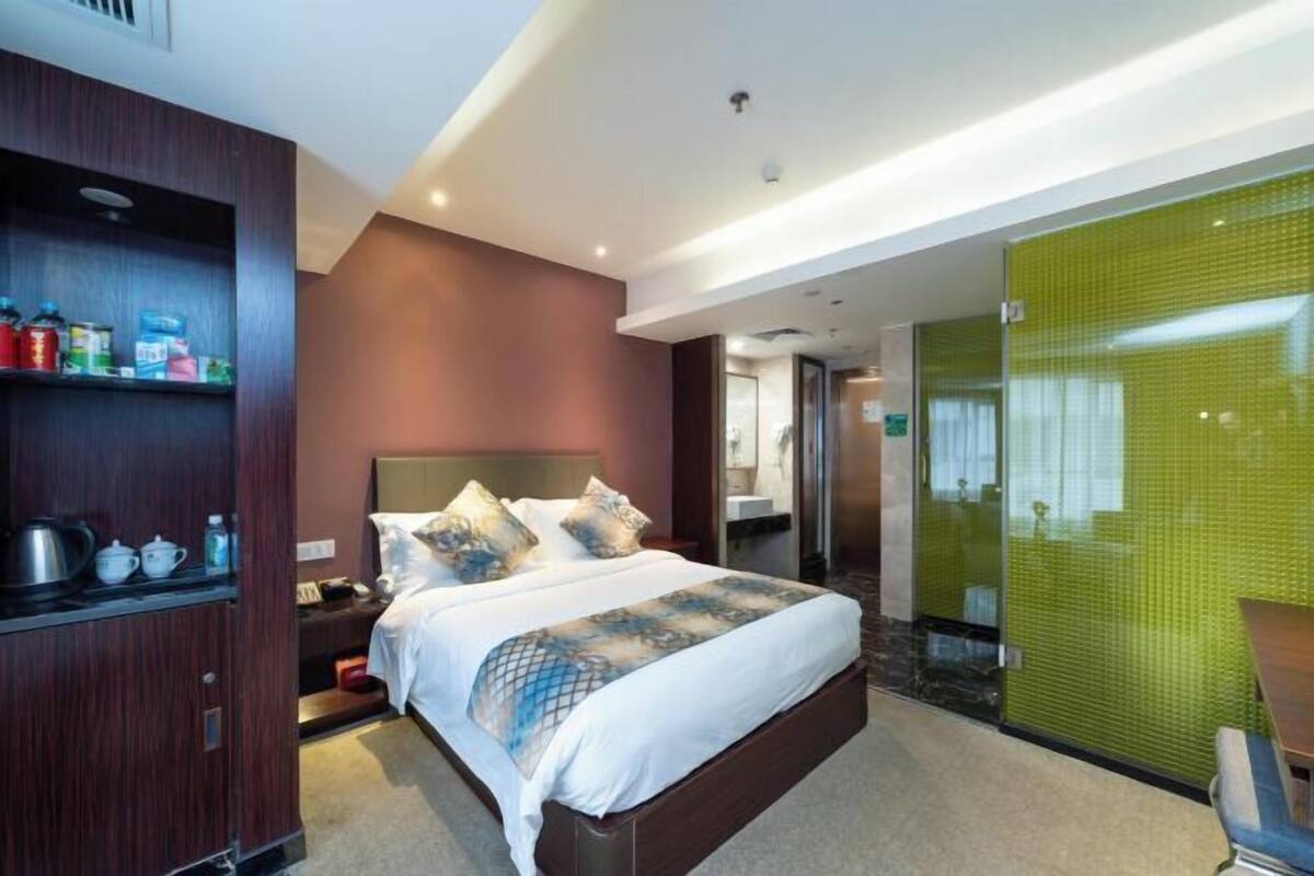 A hotel room with a large bed, a wooden wardrobe, a desk, and a green-tiled wall.