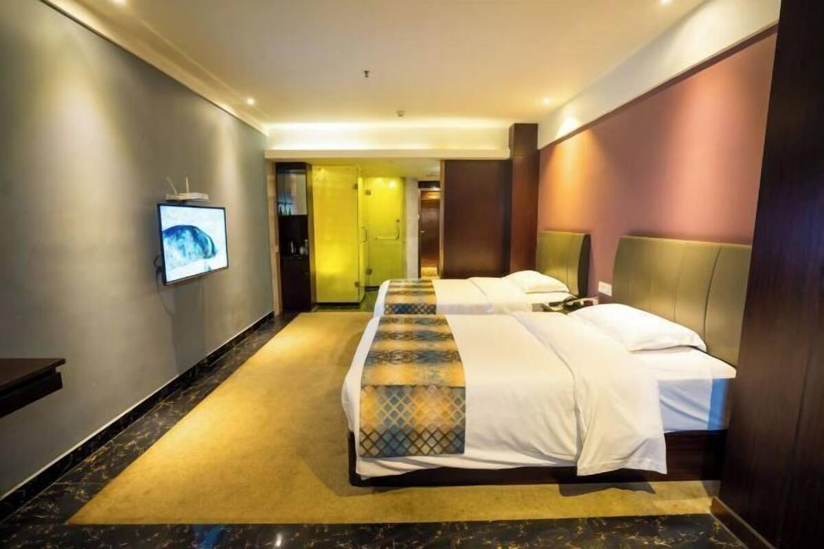 A hotel room with two beds, a television on the wall, and a carpeted floor.