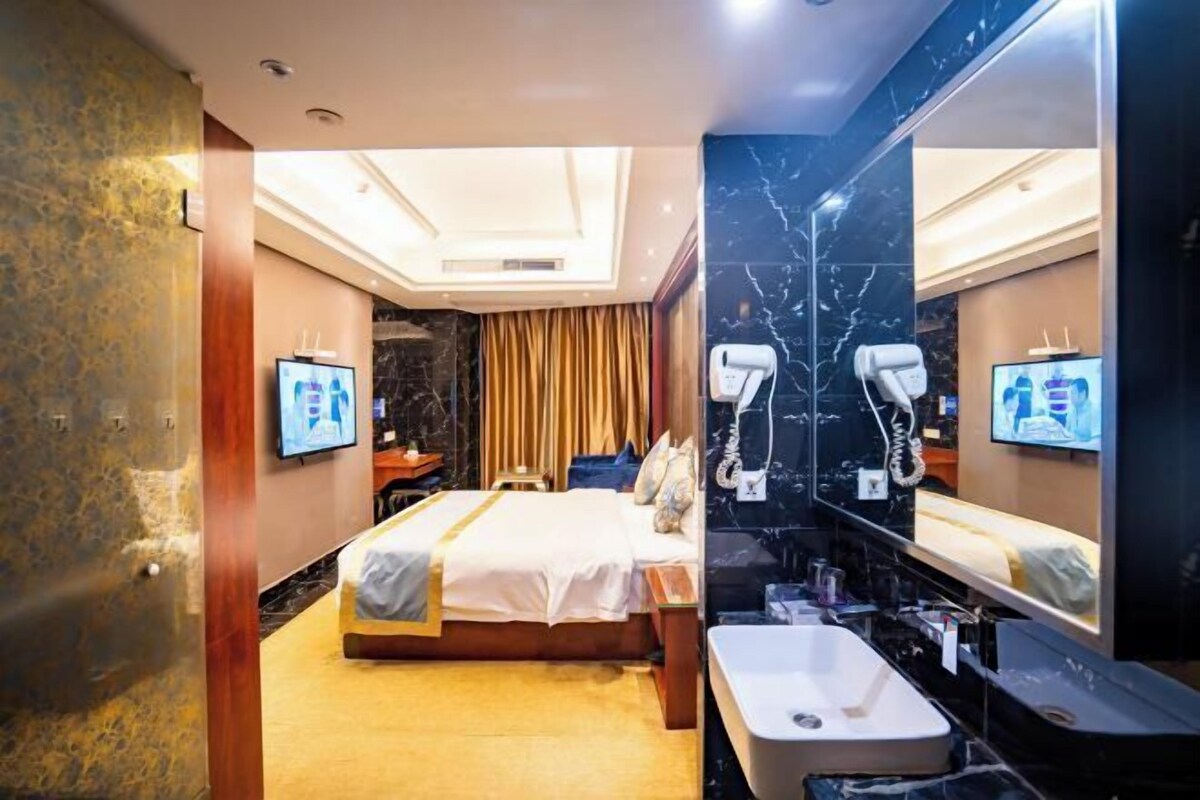 A hotel room with a bed, a large mirror, a sink, and a television.