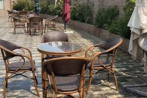 An outdoor patio with wicker furniture, including a round table and chairs, and a red umbrella.