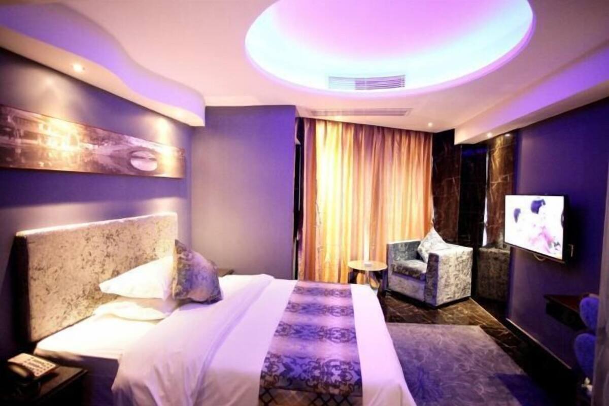 A hotel room with a bed, a chair, a television, and a ceiling light.