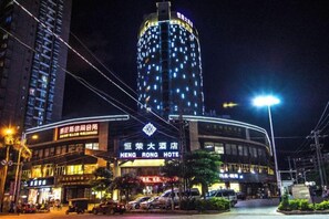 A hotel with a prominent sign, a curved facade, and a tall building with illuminated windows in the background.