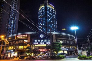 Un hotel con un letrero llamativo, una fachada curva y un edificio alto con ventanas iluminadas al fondo.