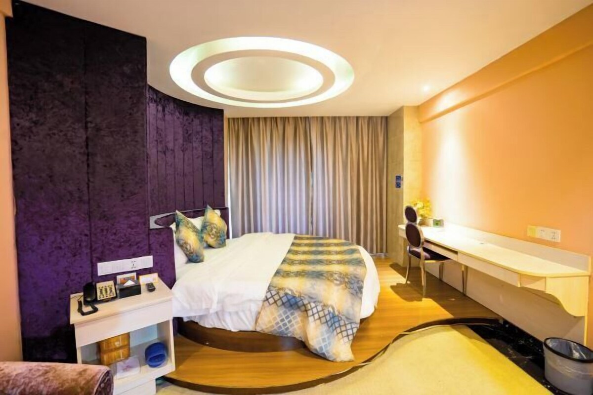 A modern hotel room with a bed, desk, and a circular ceiling light.
