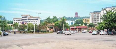 A parking lot with several cars, a building with multiple floors, and a red pagoda in the background.