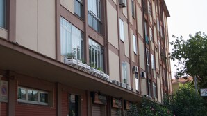 Un immeuble résidentiel à plusieurs étages, doté de balcons, d’un petit espace jardin et d’une entrée bien visible.