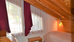 Una camera da letto con soffitto spiovente, un letto, un piccolo tavolino e una finestra con tende leggere e un lampadario a forma di stella.