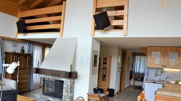 Un intérieur rustique avec une cheminée en pierre, des étagères en bois, un coin cuisine et un espace repas.