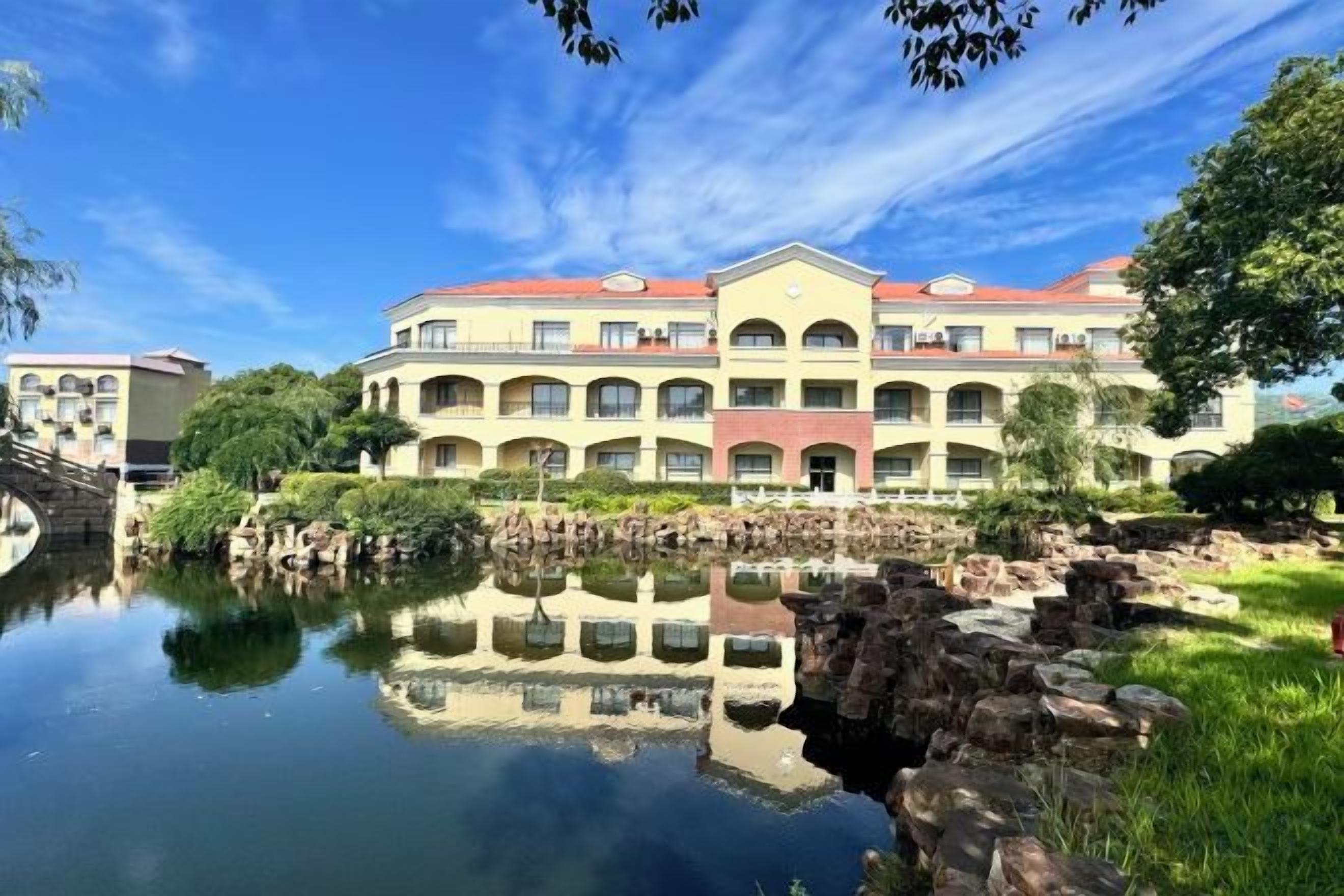 A multi-story hotel with a reflection in the water, a stone bridge, and a red roof.